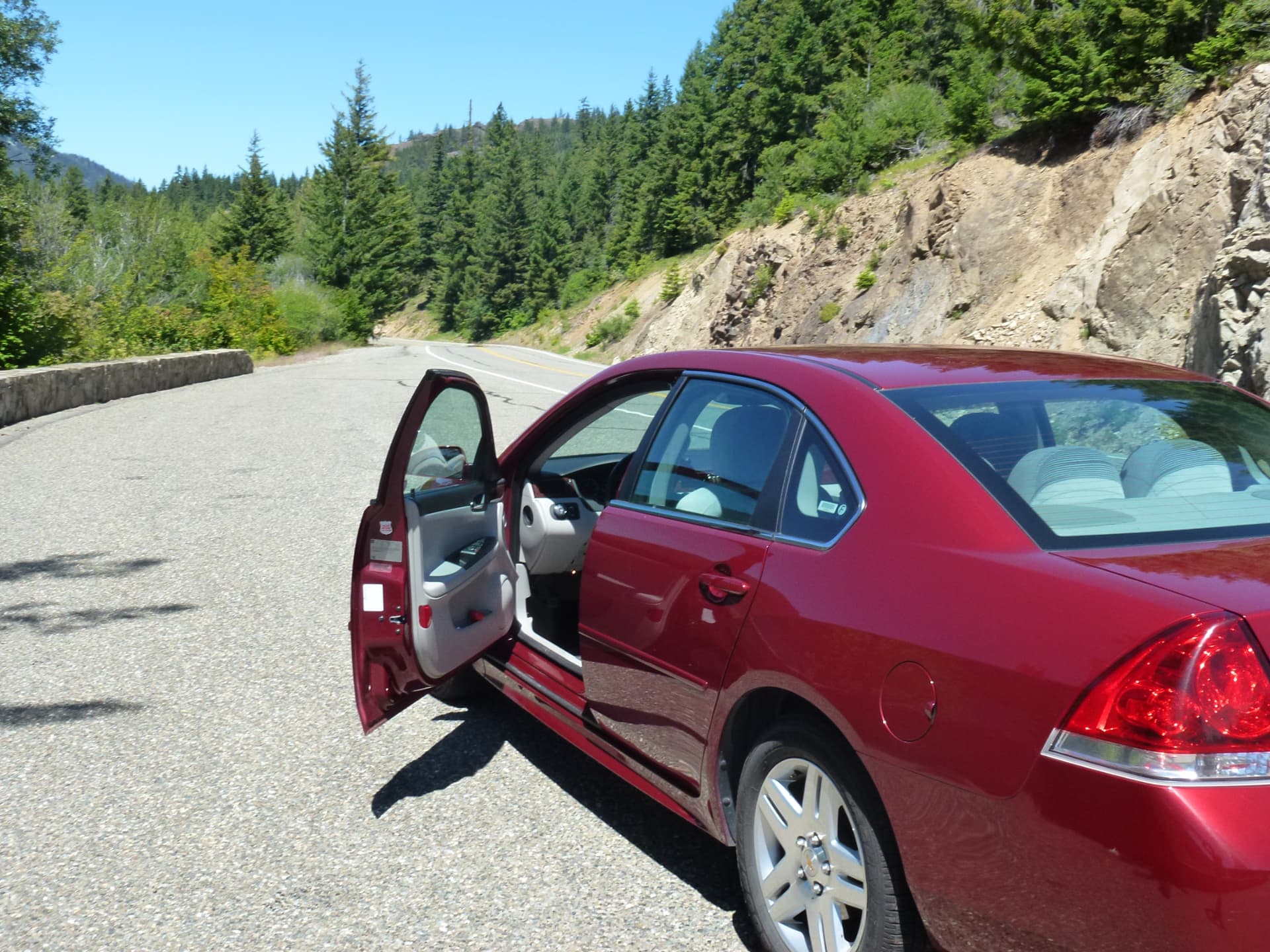Rode Chevrolet Impala met open deur langs een bergweg