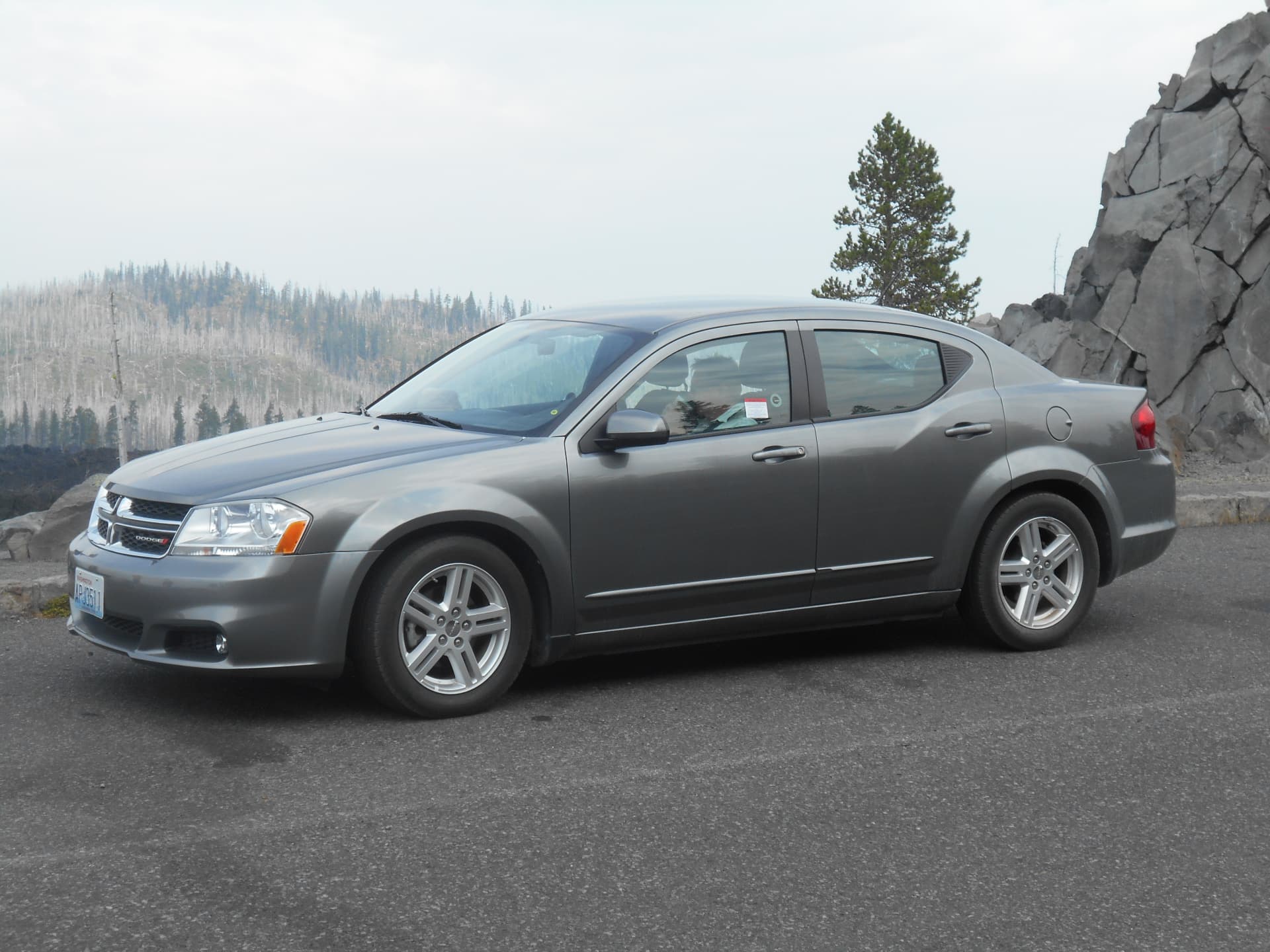 Grijze Dodge Avenger huurauto bij een uitzichtpunt in de bergen